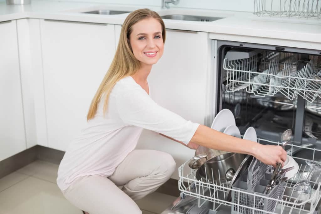 Smiling gorgeous model kneeling next to dish washer in bright kitchen Smiling gorgeous model kneeling next to dish washer in bright kitchen