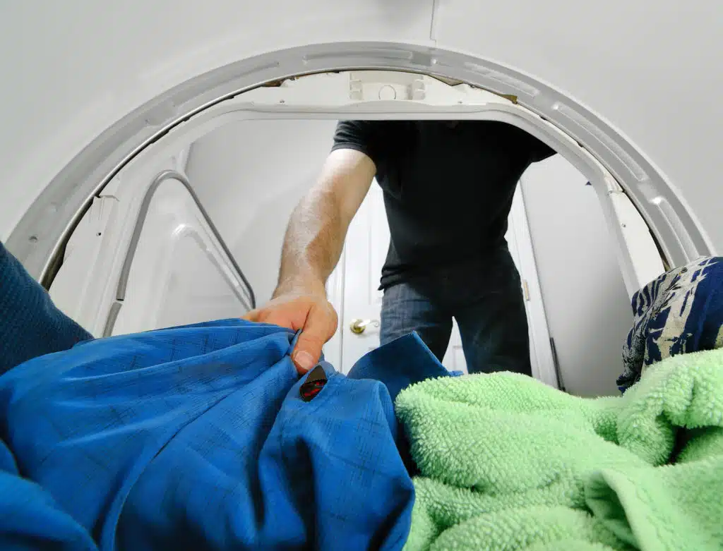 Man reaching into a dryer to pull out laundry.