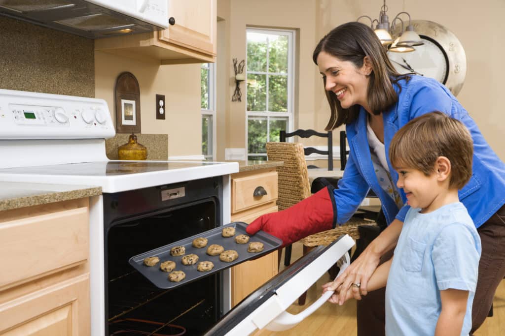 Side view of Hispanic mother and son putting cookies into oven. Side view of Hispanic mother and son putting cookies into oven.